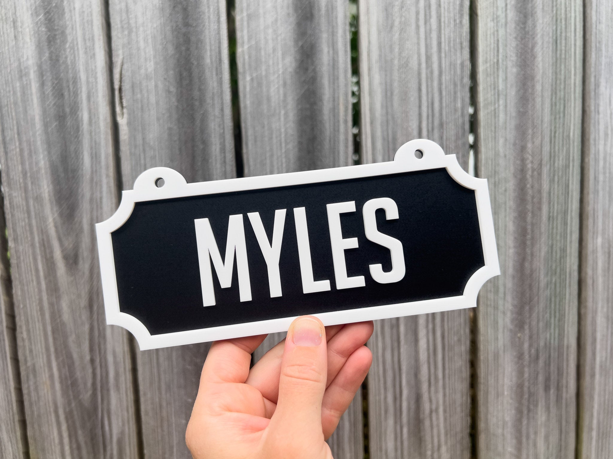 Hand holding a sign with 'MYLES' text against a wooden fence background  | Coji Designs