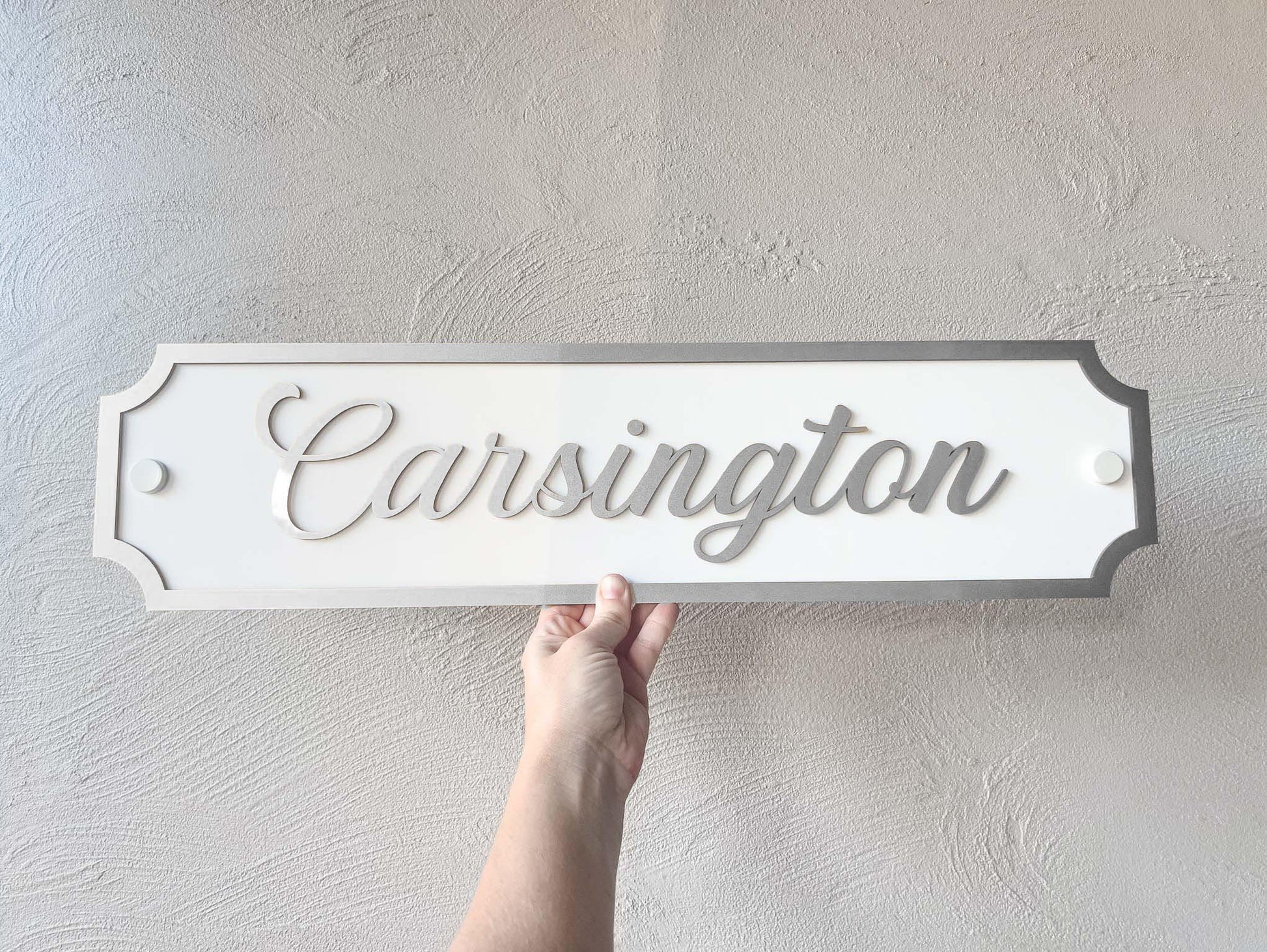 A elegant script style 3D acyrlic sign featuring the word 'Carsington' in metallic silver on a white sign.