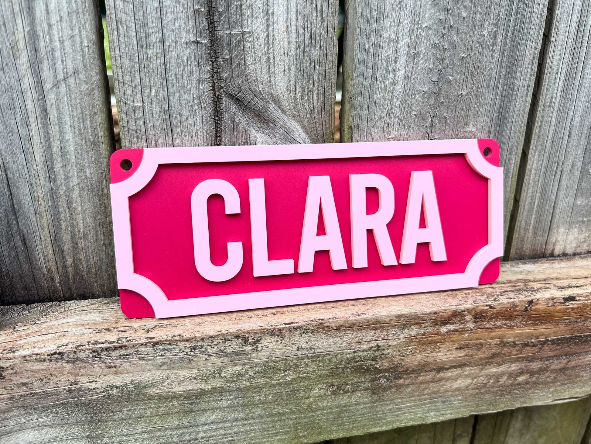 Pink sign with 'CLARA' on a wooden surface