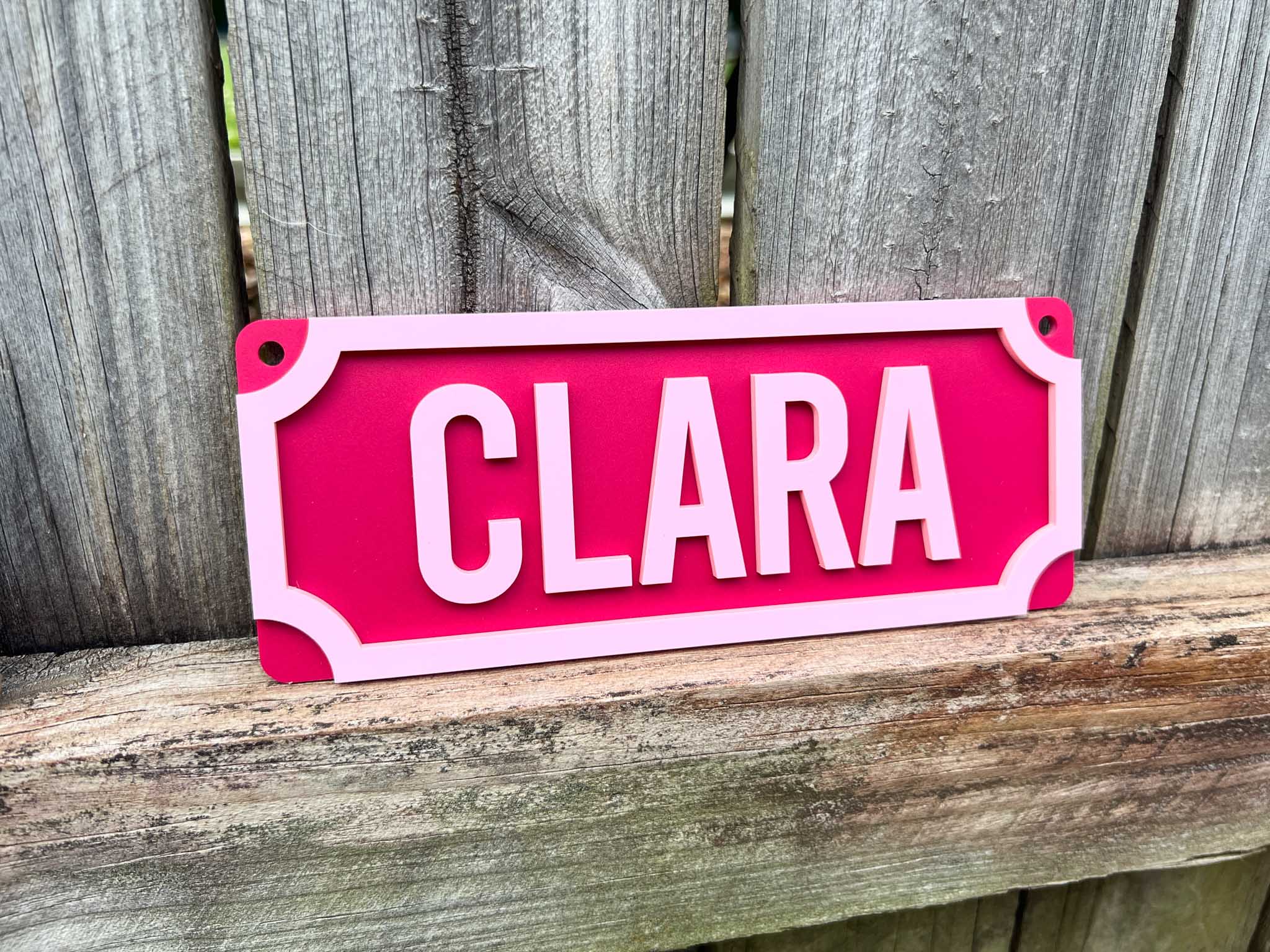 Pink sign with 'CLARA' on a wooden surface