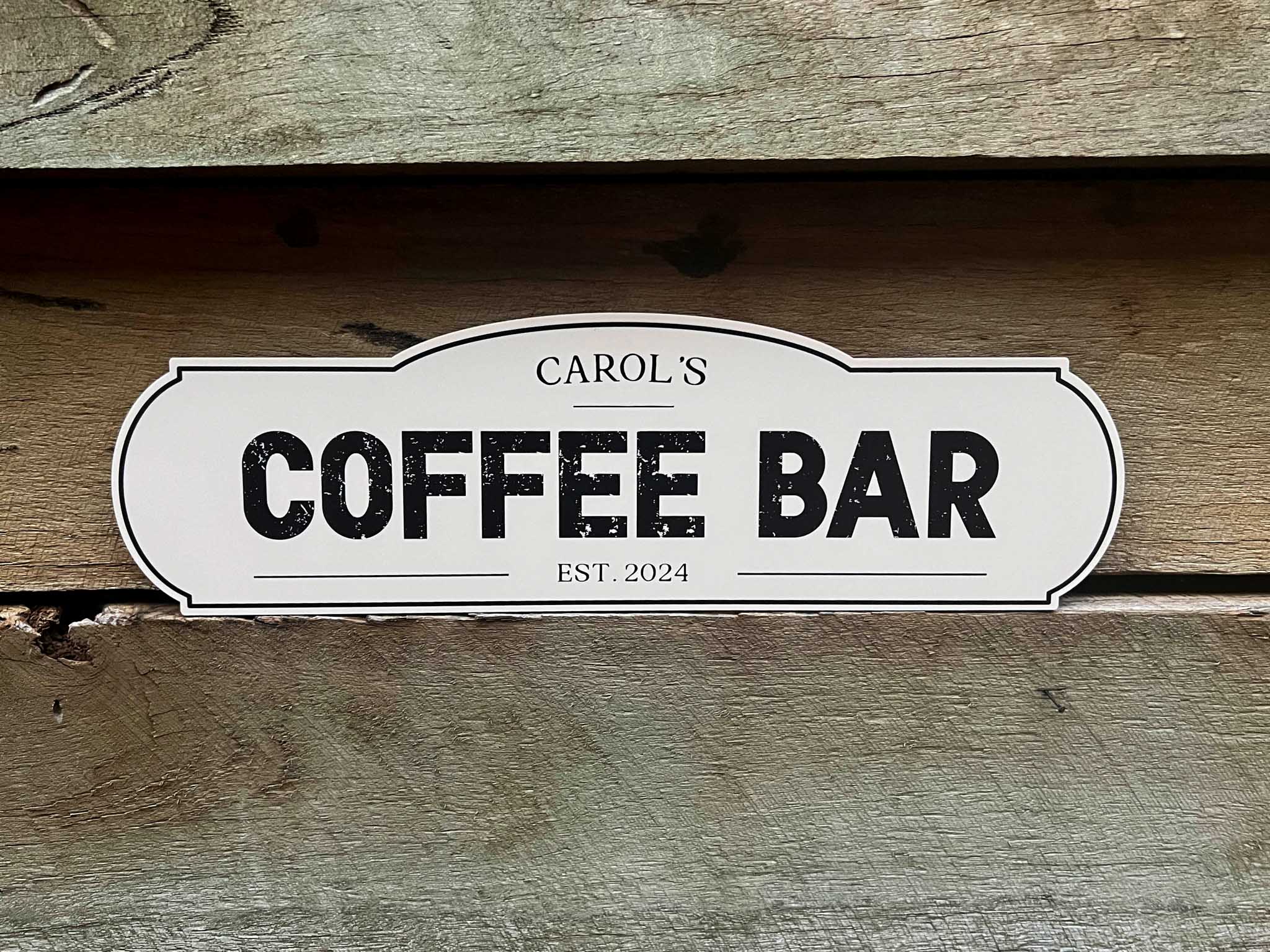 A beige and black coffee bar sign sitting on a wooden wall.