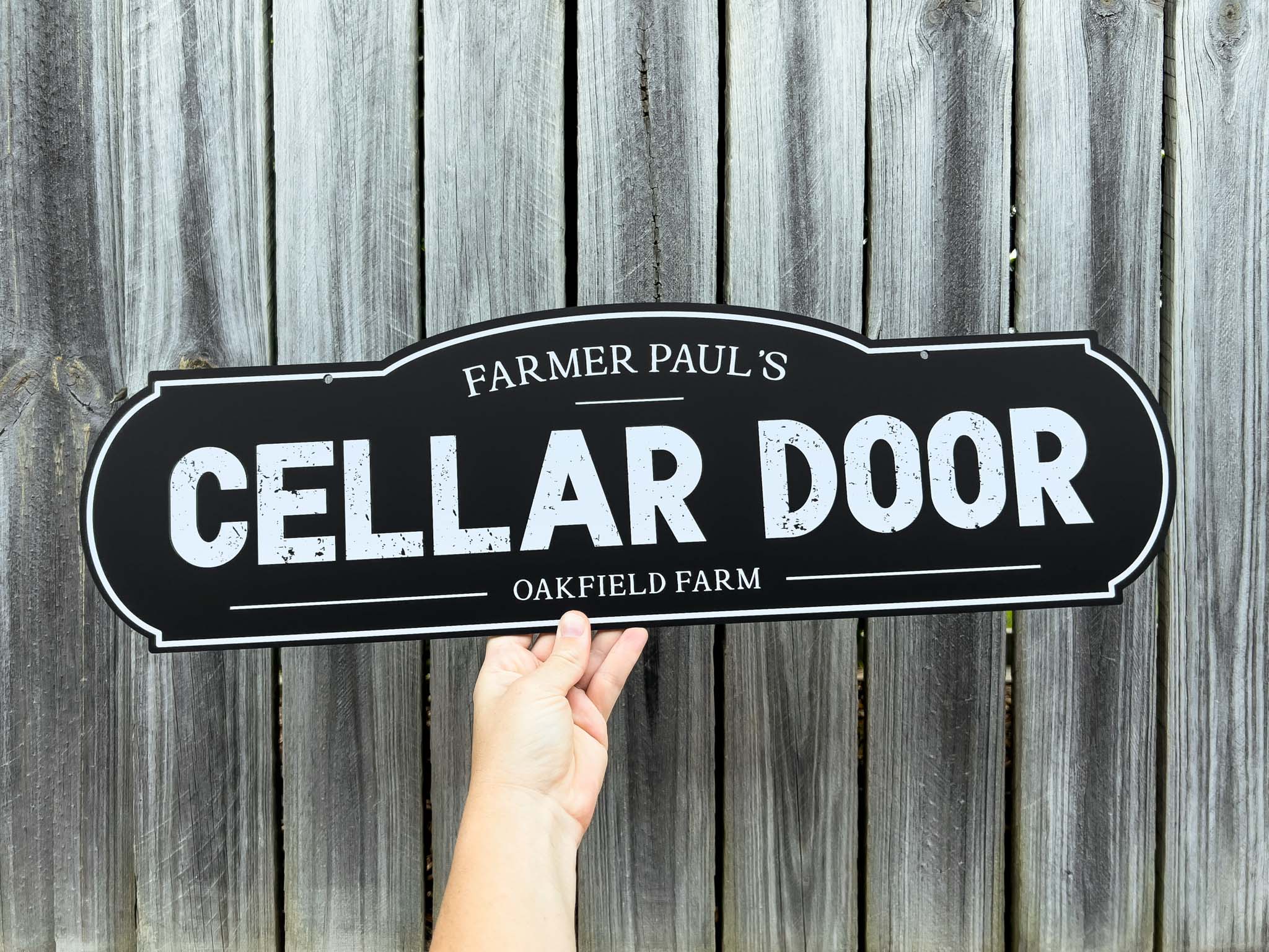 A black and white custom distressed vintage sign that reads 'Farmer Paul's Cellar Door'.