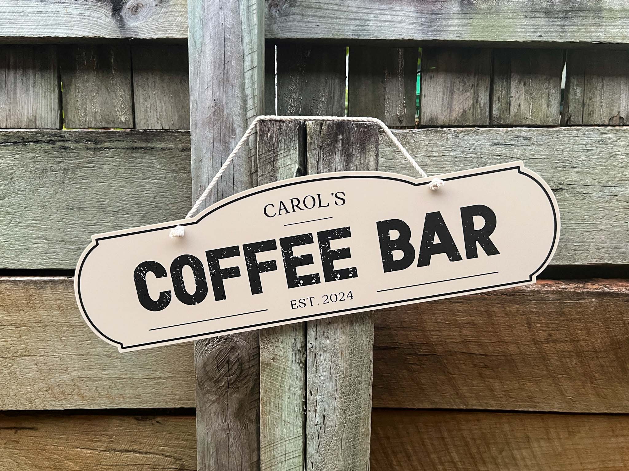 Custom printed beige and black distressed text sign that says 'Carol's Coffee Bar Est. 2024'.